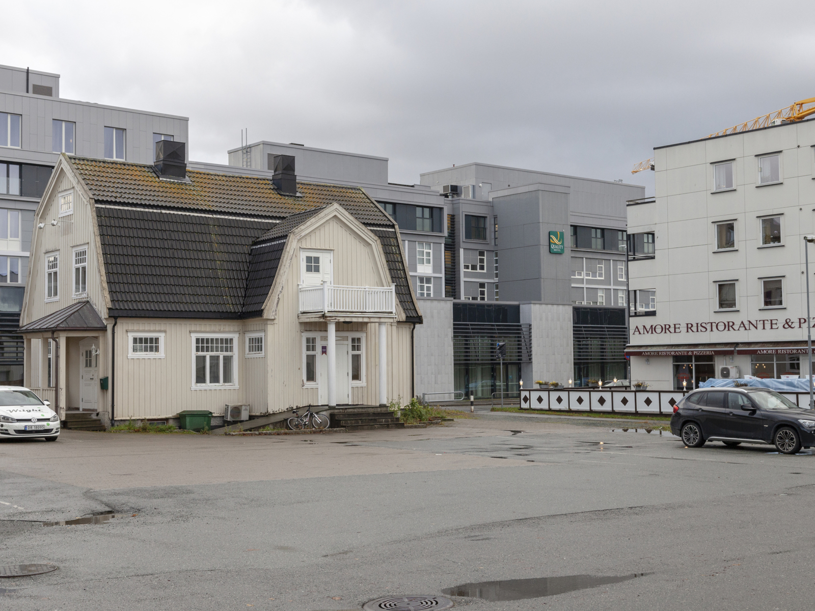 Et trebygg blant andre større nyere bygg. Foto.