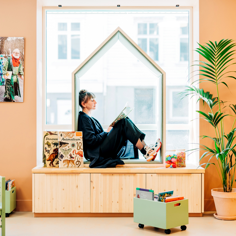 Interiørfoto av vinduskarm i bibliotek, en kvinne sitter og leser.