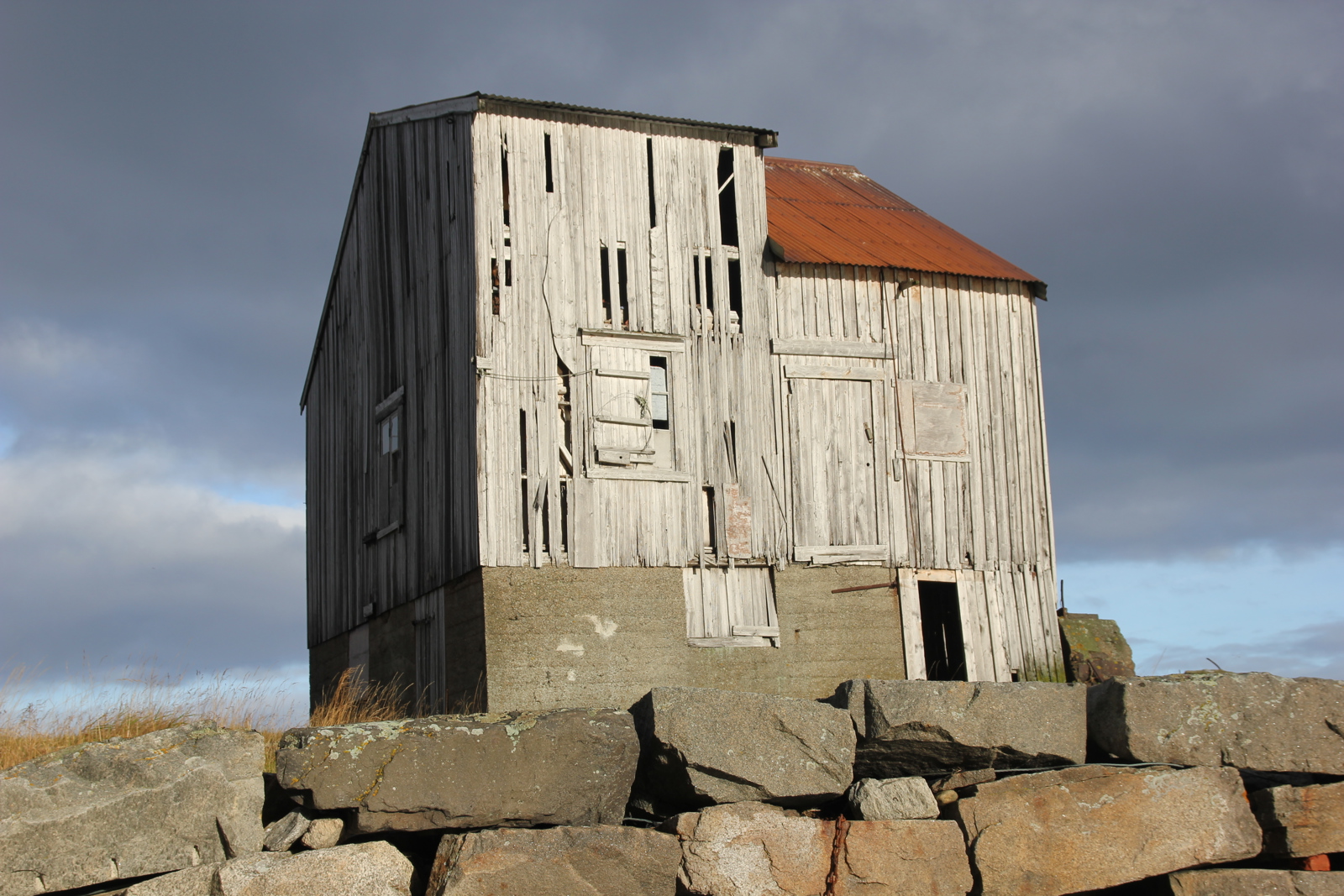 Foto av nedslitt grånet hus, steinmur i forkant.