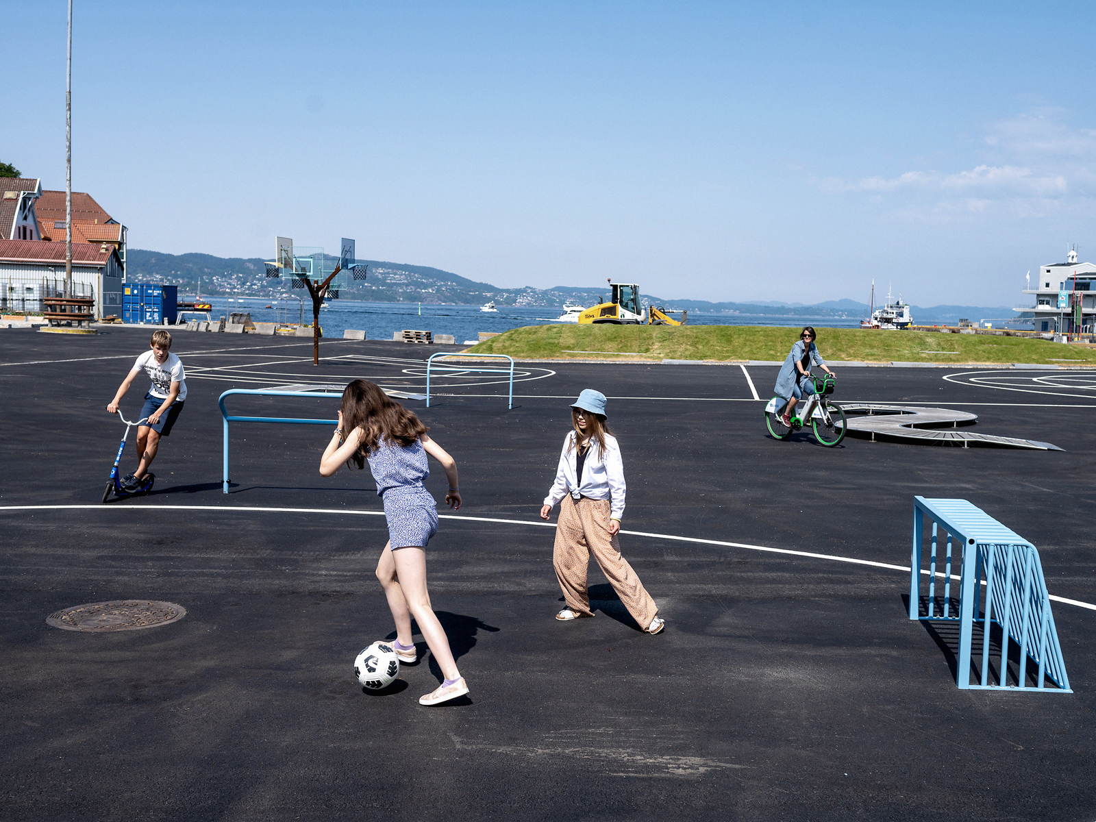 Barn leker på en stor plass utendørs, noen spiller fotball, andre sykler. Foto.