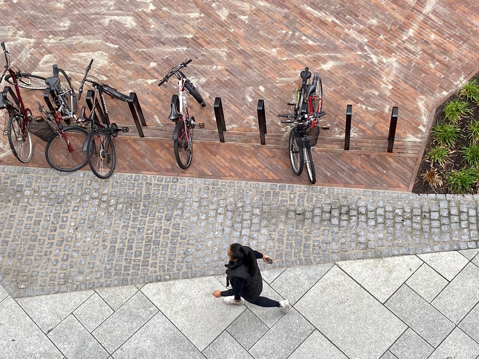 Foto av bygulvet ovenfra, en mann som går, sykkelparkering og ulike typer stein i bygulvet.