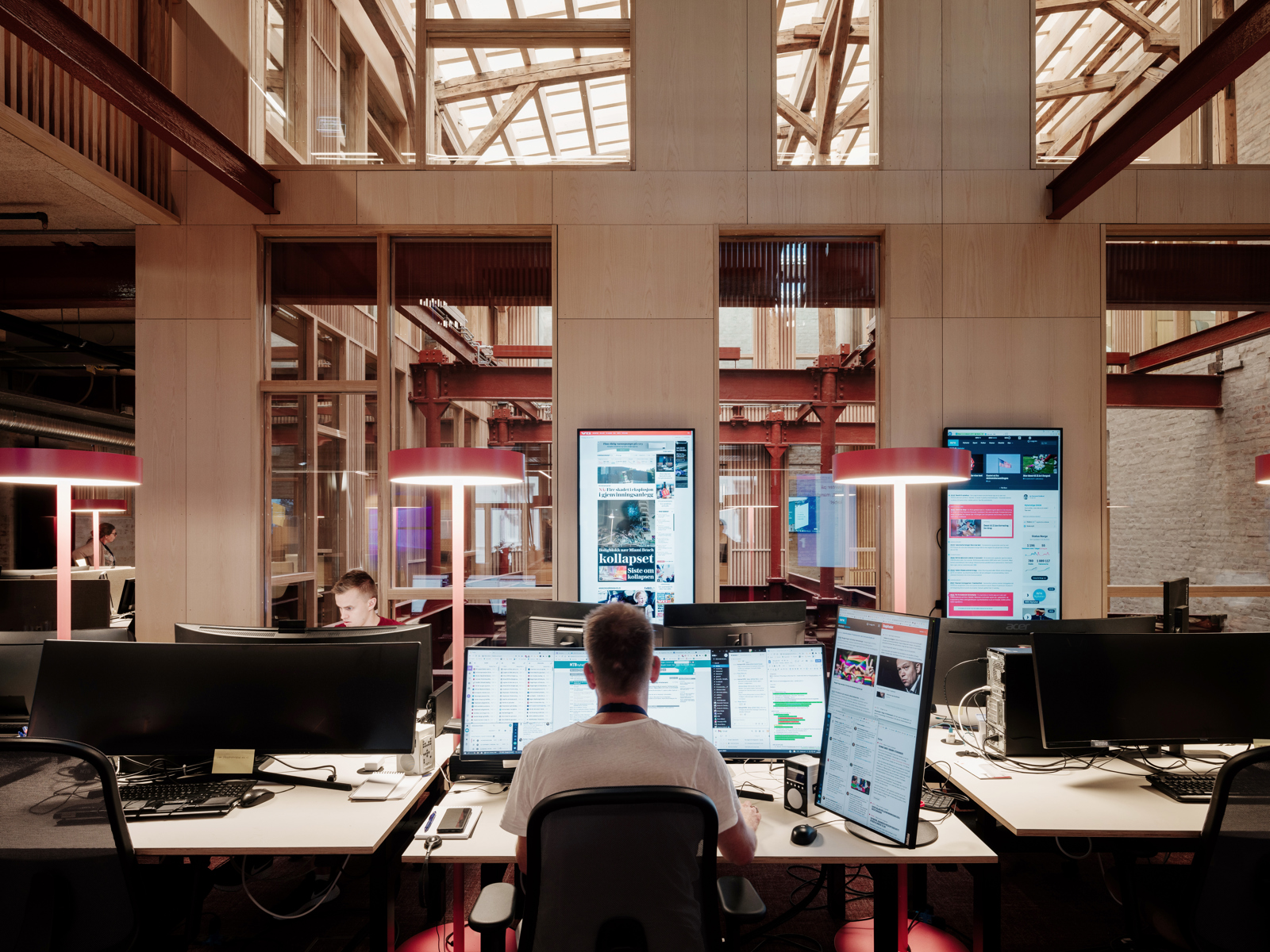 En mann sitter og jobber fremfor mange skjermer, i pressens hus. Foto.