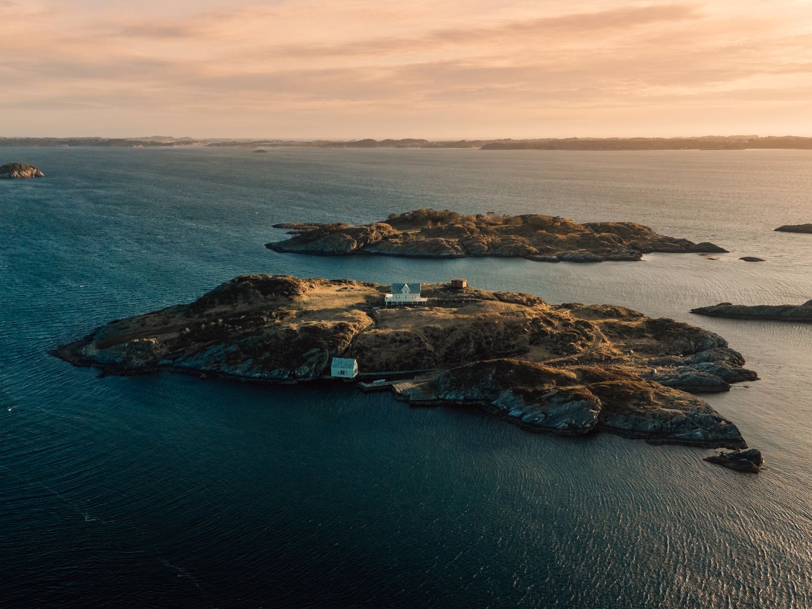Drone foto av en øy med to hus på, hav og mindre øyer rundt.