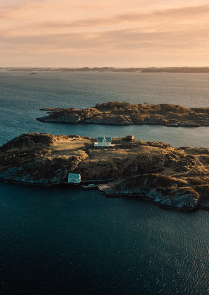 Drone foto av en øy med to hus på, hav og mindre øyer rundt.