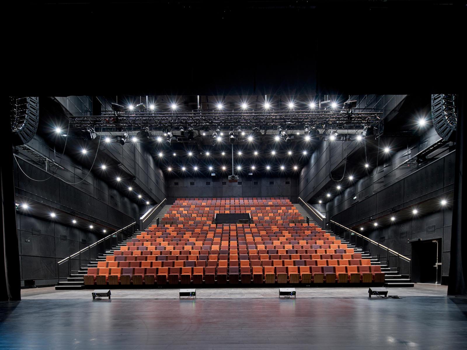 Interiør foto fra scenen på Steinkjær kulturhus og ut på publikums amfiet i røde toner, ellers er alt svart