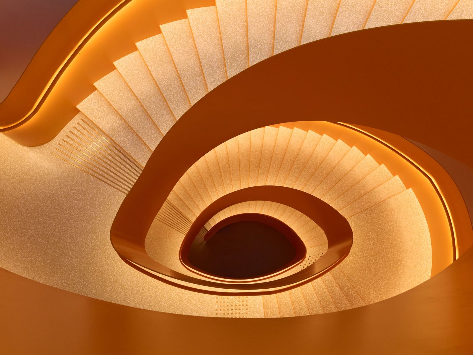 Interiør foto sett ned en organisk formet trapp, opplyst av varmt lys langs gelenderet.