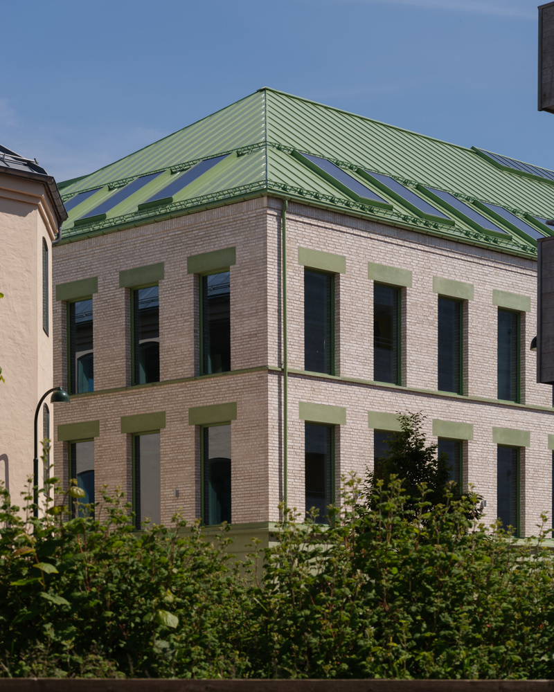 Foto av hjørne på mursteinsbygg med grønt tak og grønne detaljer.