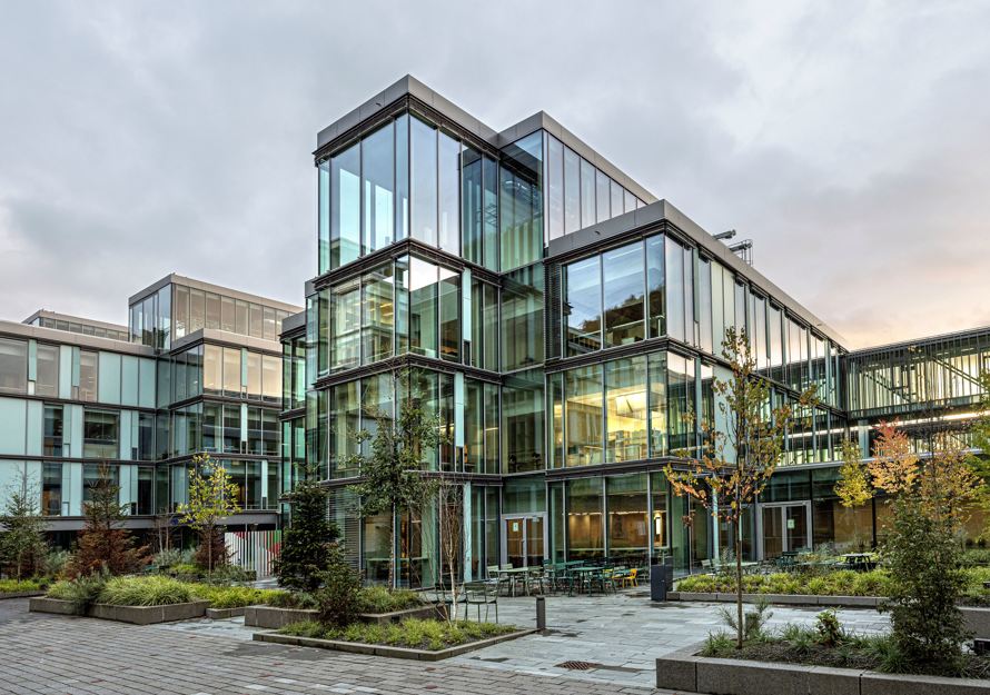 Foto av fasaden på Glasblokkene, vegetasjon og hardt underlag på plassen fremfor.