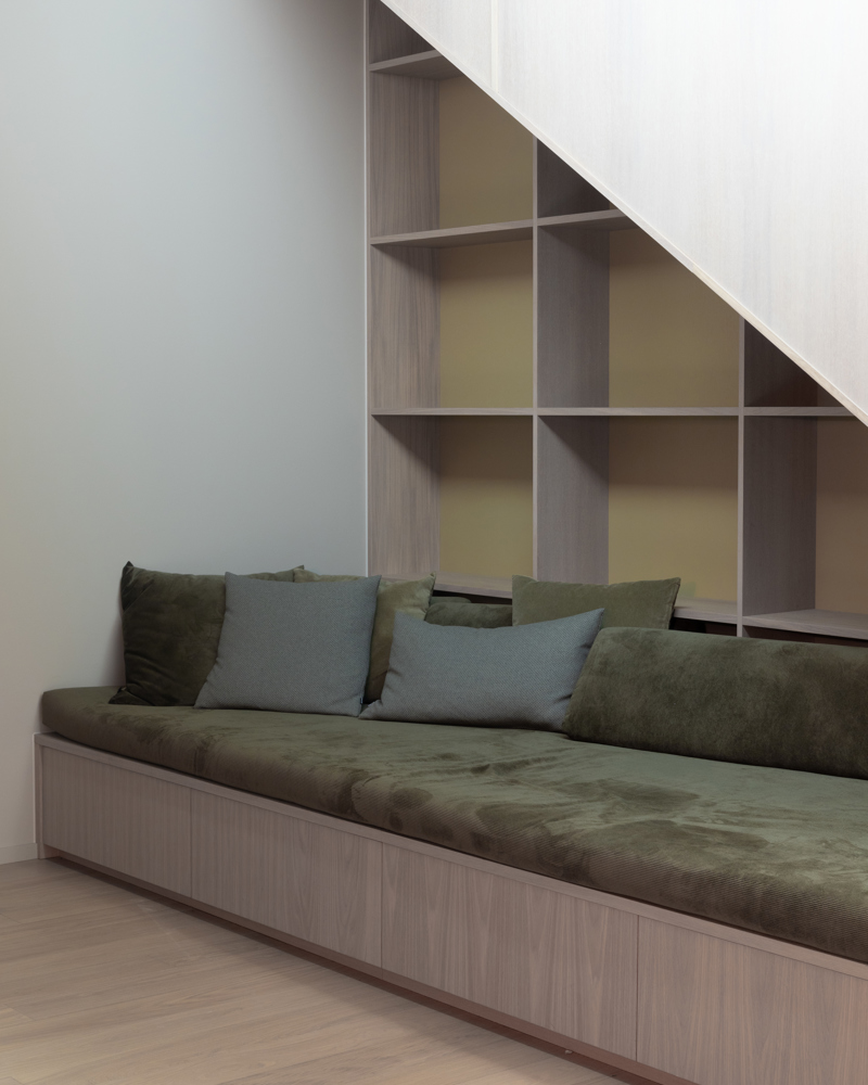 Innebygd sofa under trapp med puter i og hyller bak. Interiør. Foto.