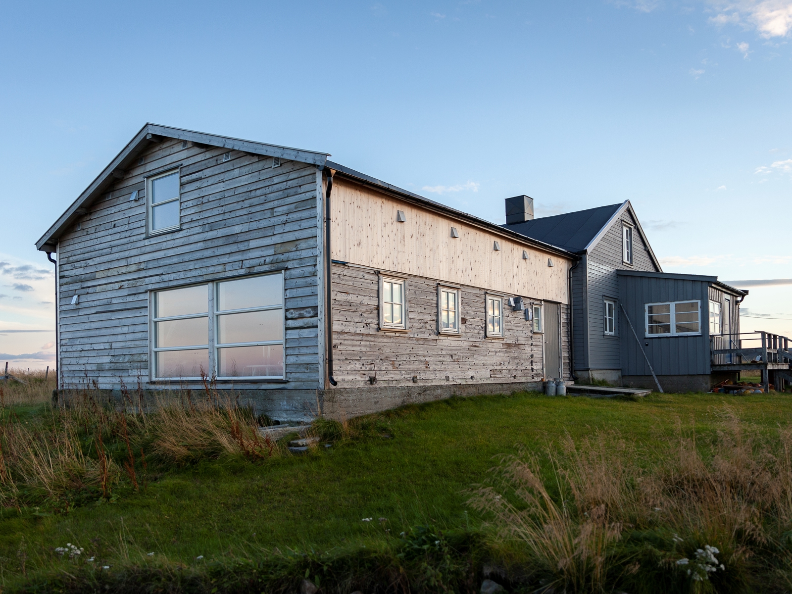 Foto av grått bygg med ny og gammel bygg i grønt landskap.