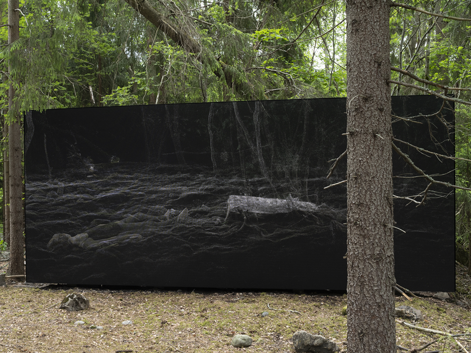 Kunstverk i form av en stor svart firkant står midt i skogen. Foto.