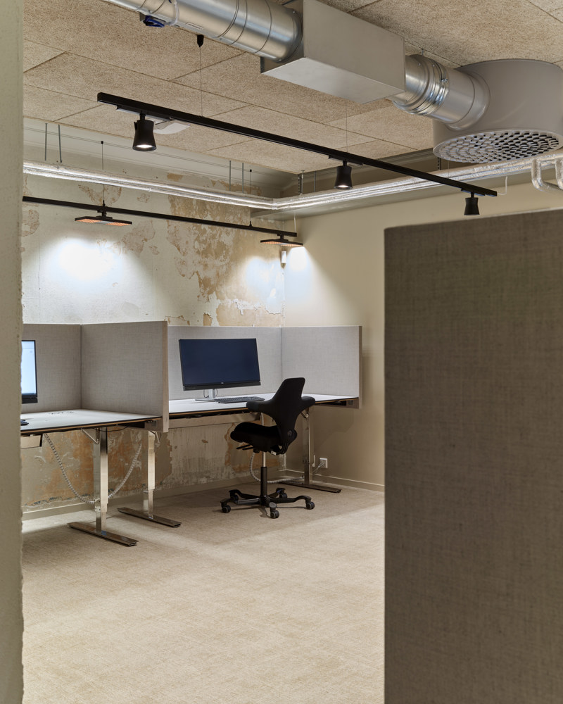 Interiørfoto som viser pulter i åpent kontorlokale, synlig ventilasjon i taket.