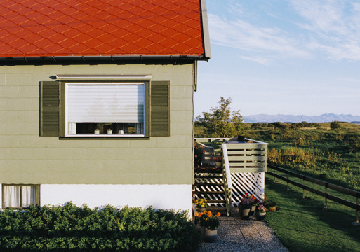 Foto av et hus med rødt tak og eternittplater på fasaden.