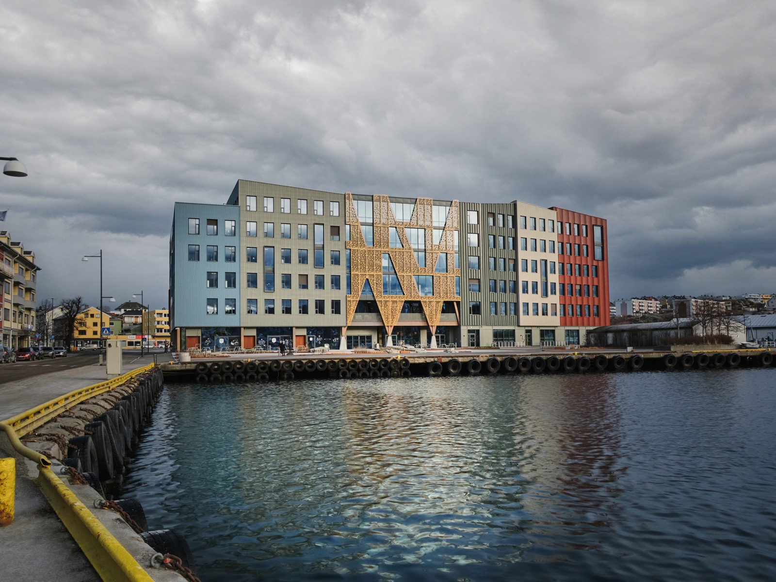 Fasade foto av Campus Kristiansund på kaikanten, oppdelt fasade med mange ulike kledninger, vann i forgrunnen.