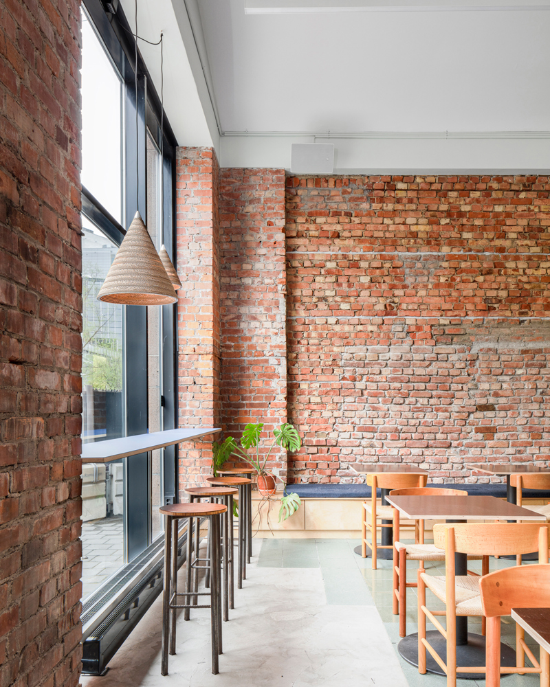 Interiør, vegger av rød tegl, stoler langs vinduet og sittegrupper i rommet. Foto.