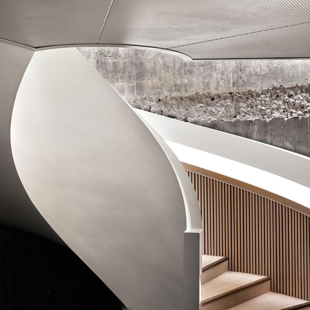 Interiørfoto av spiraltrapp i betong og treverk.