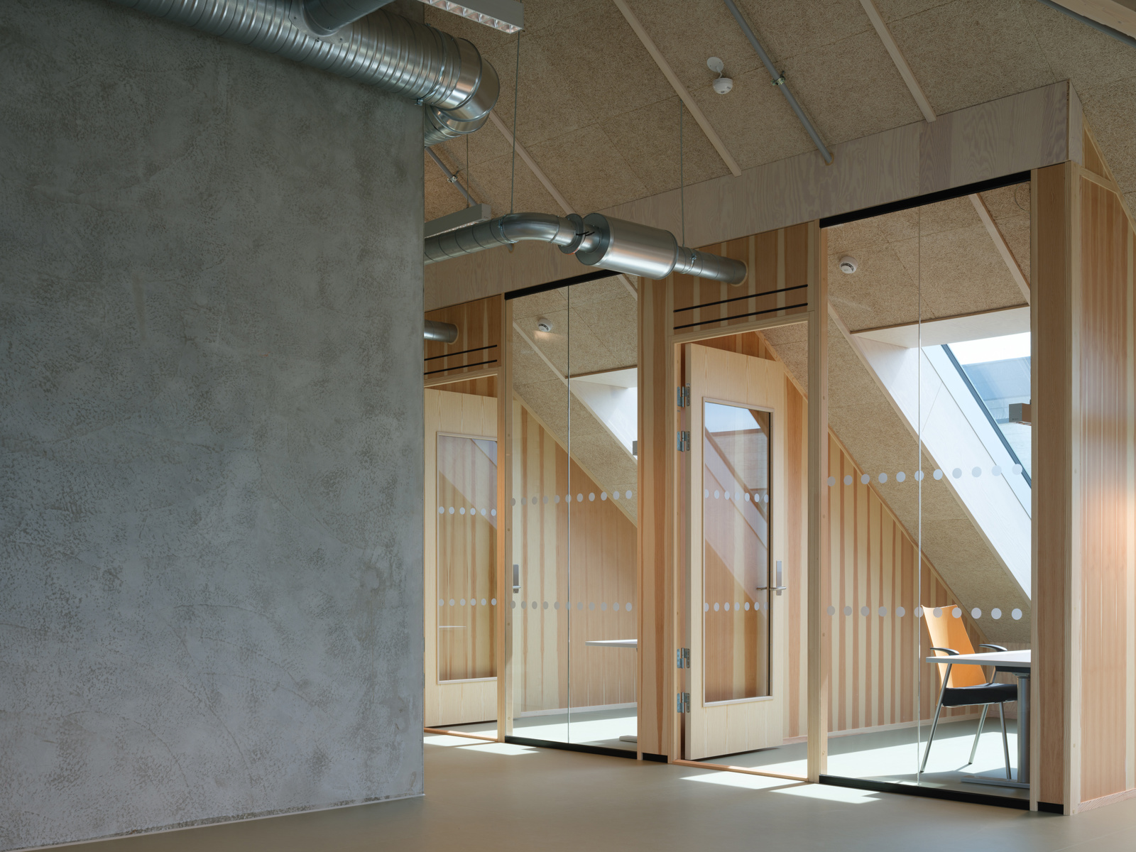 Interiør foto av kontorlokale med cellekontorer i treverk og glass, betong kjerne.