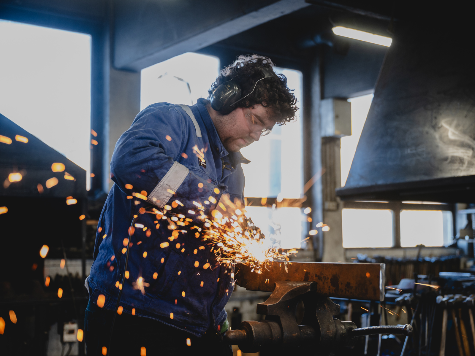 Foto av en mann som står på et verksted og jobber med jern, gnistene flyr.