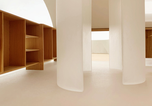 Interiør, preget av hvite plater og halvsirkel vegger i midten av rommet, tremøbler. Foto.