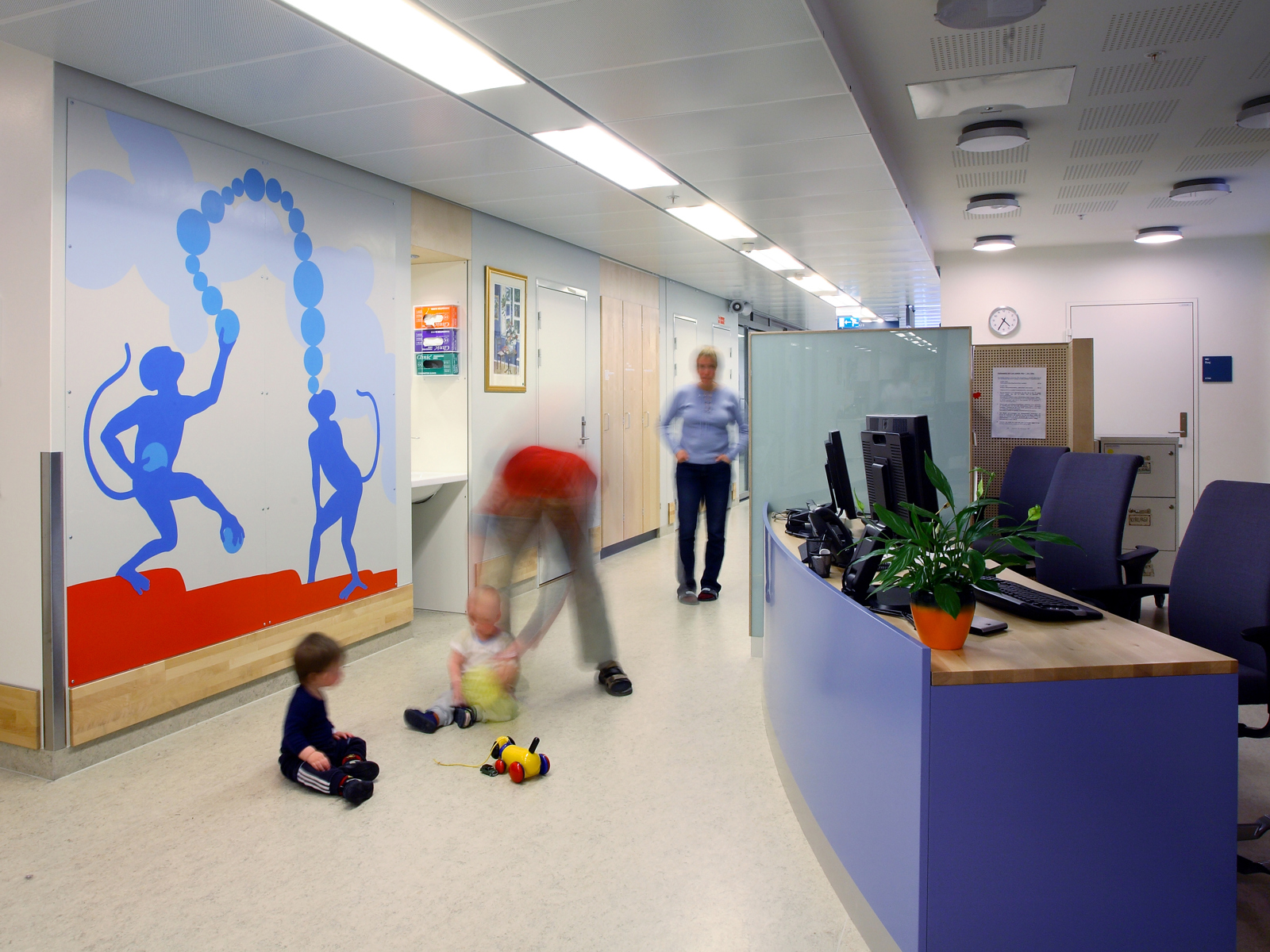 Interiør foto av gang på sykehus der et barn leker med en voksen på gulvet.