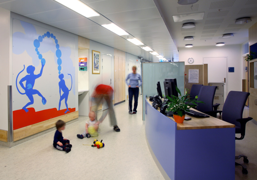 Interiør foto av gang på sykehus der et barn leker med en voksen på gulvet.