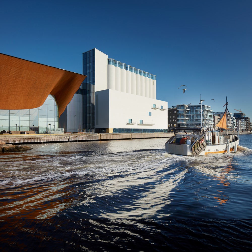 Foto av Kunstsiloen i Kristiansand i kontekst, vann og båt i forgrunnen.
