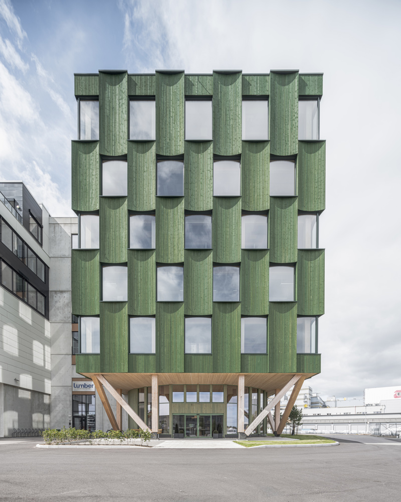Foto av grønn fasade av treverk i bykontekst.