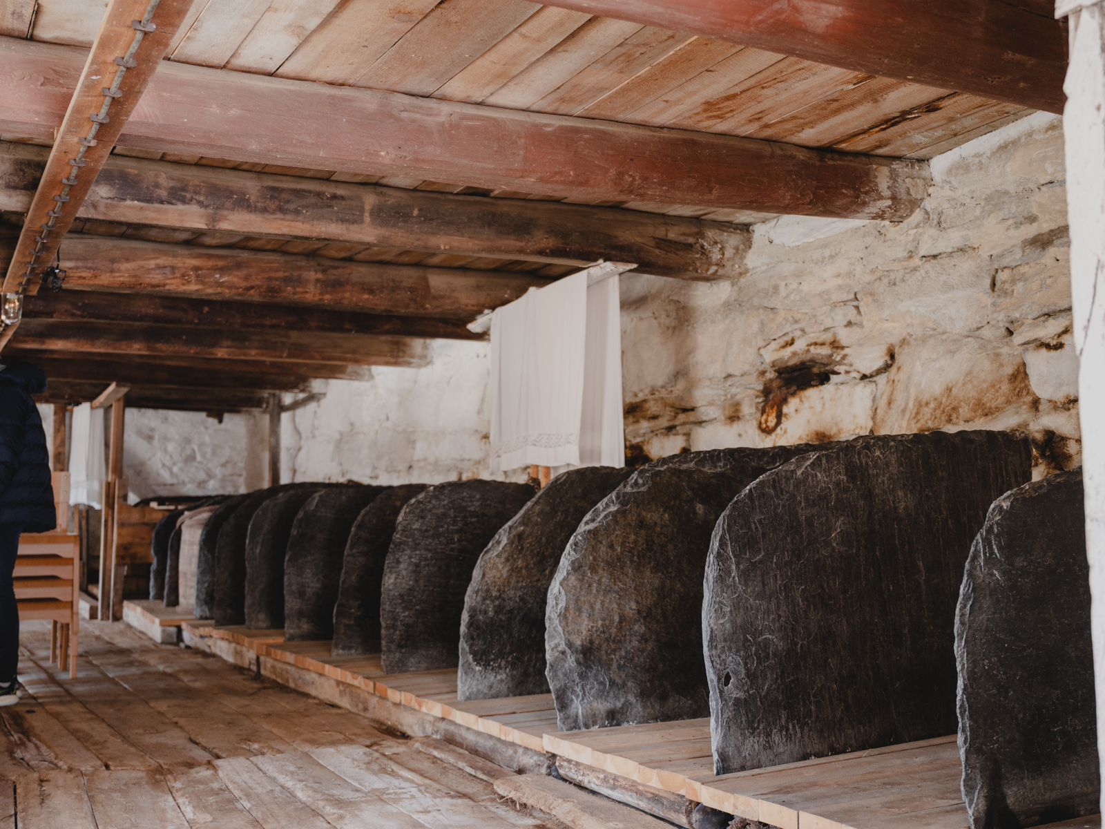 Foto av et fjøs med skiferheller som skiller båsene fra hverandre.