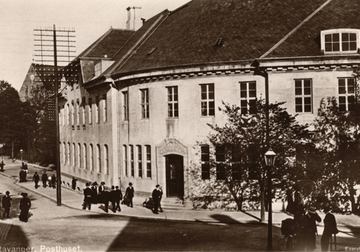 Bygg i et veikryss, mange mennesker i gata, sepia. Foto.